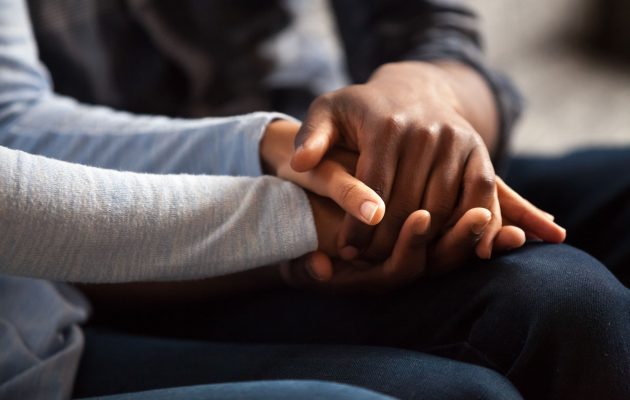 Two people sharing a quiet, comforting moment - one set of hands clasped over another